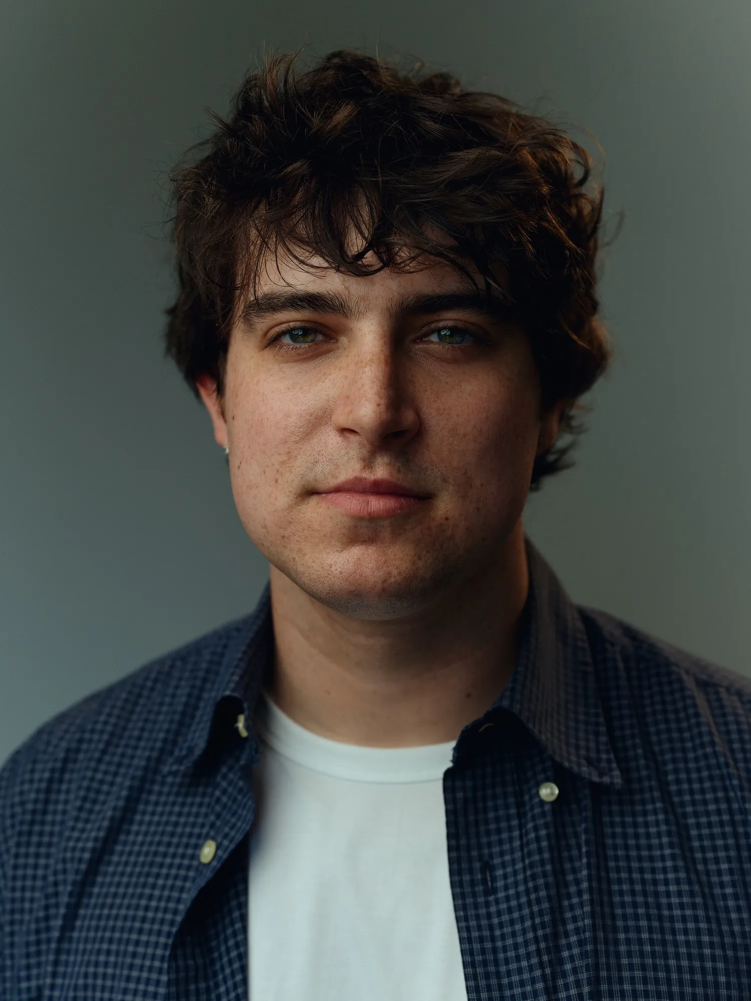 Portrait of Sam Astra in a navy plaid shirt against a gray backdrop